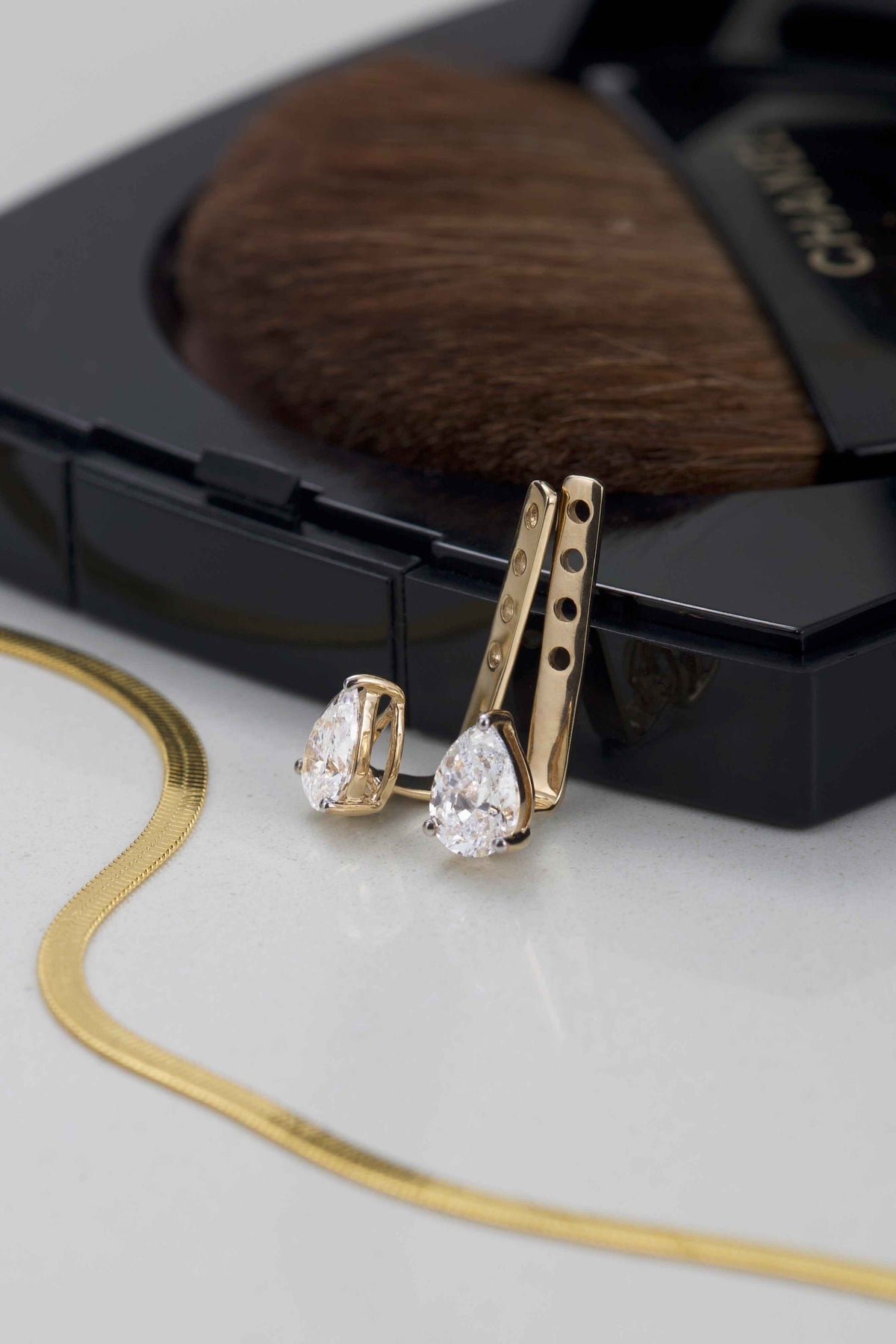 Gold earrings with pear-shaped gemstones on a Chanel makeup compact background