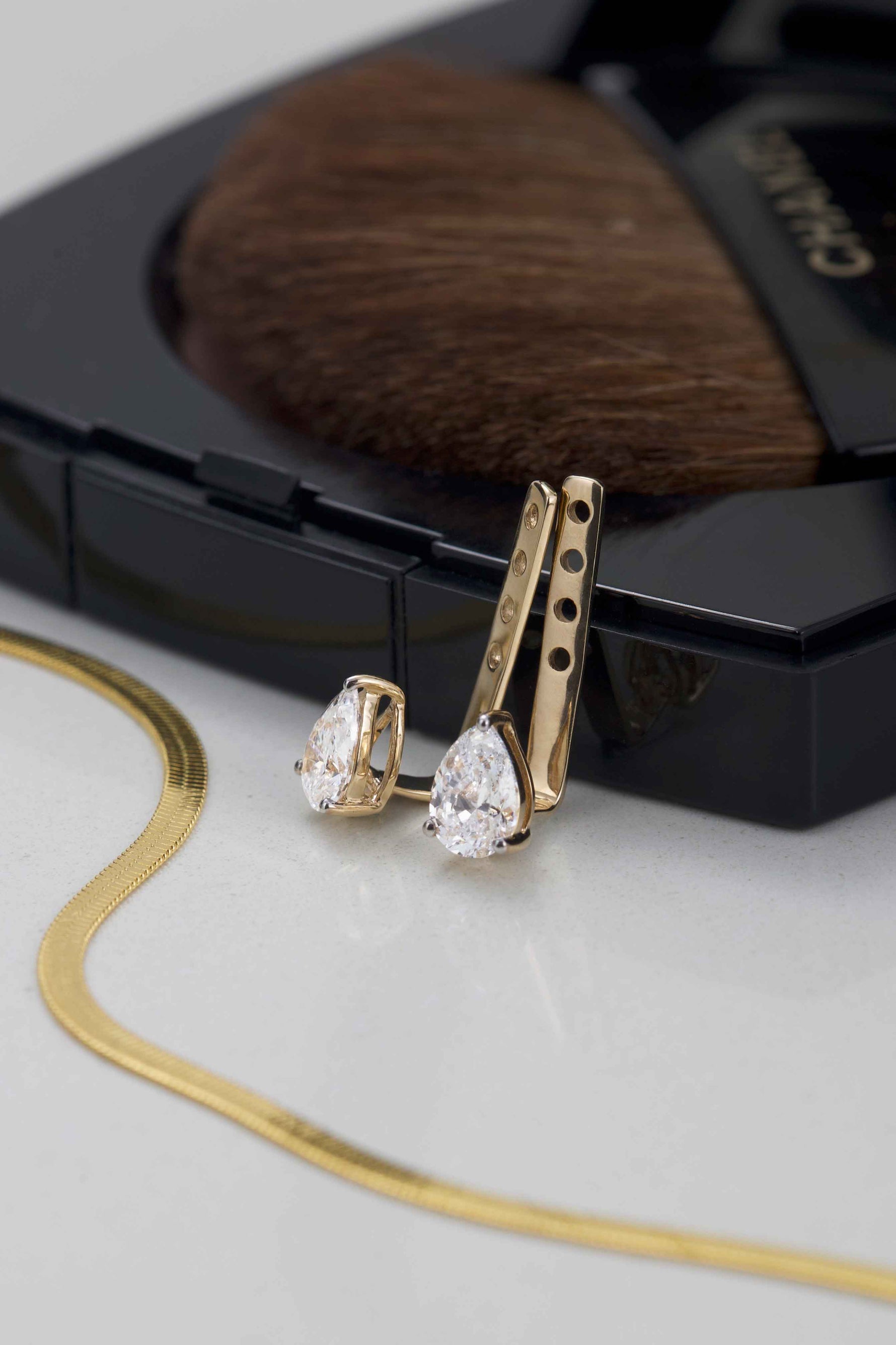 Gold earrings with pear-shaped gemstones on a Chanel makeup compact background