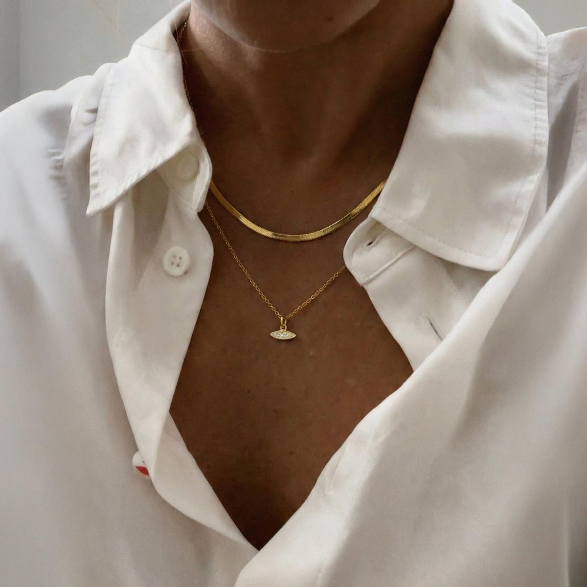 Close-up of a person wearing a gold necklace with a white shirt.