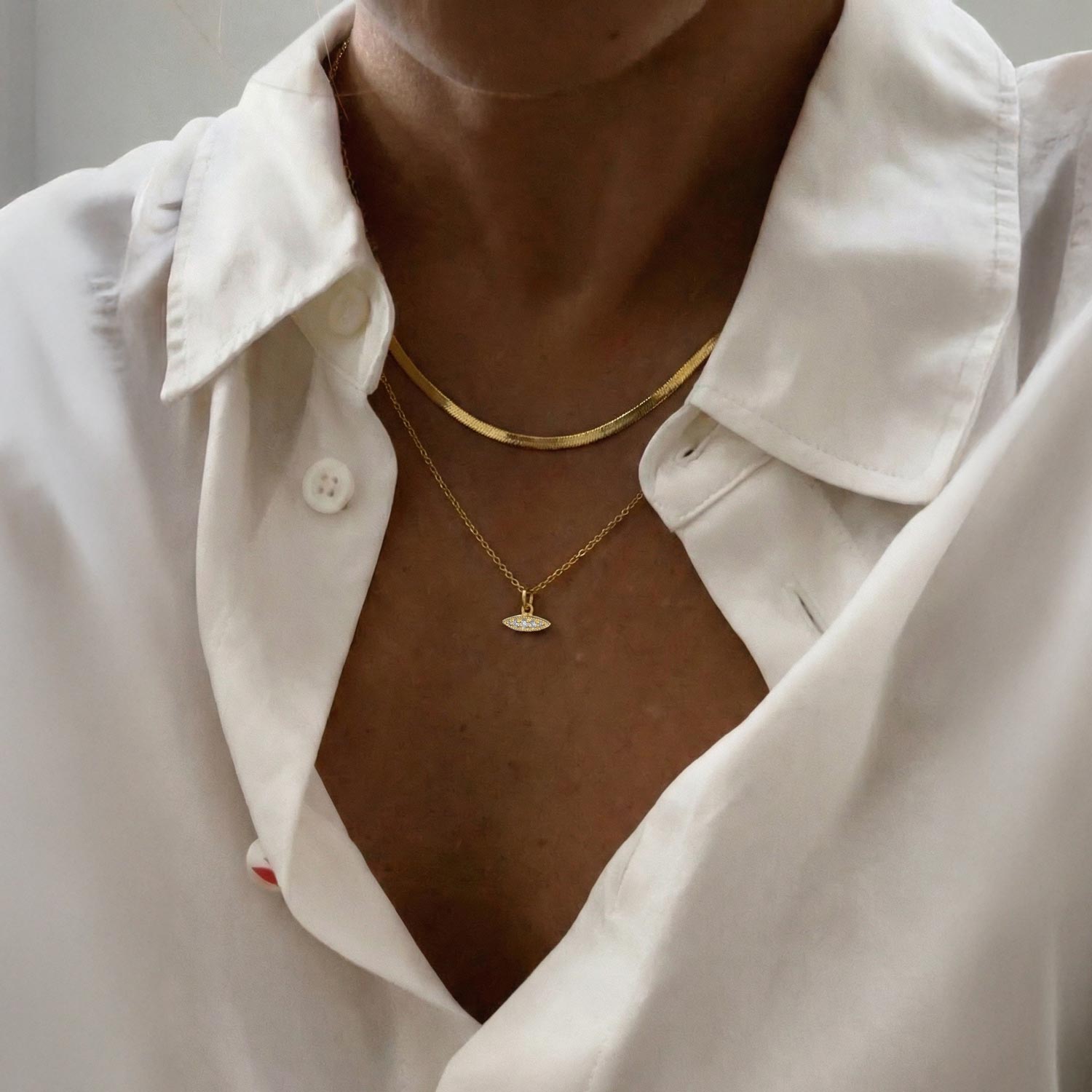Close-up of a person wearing a gold necklace with a white shirt.