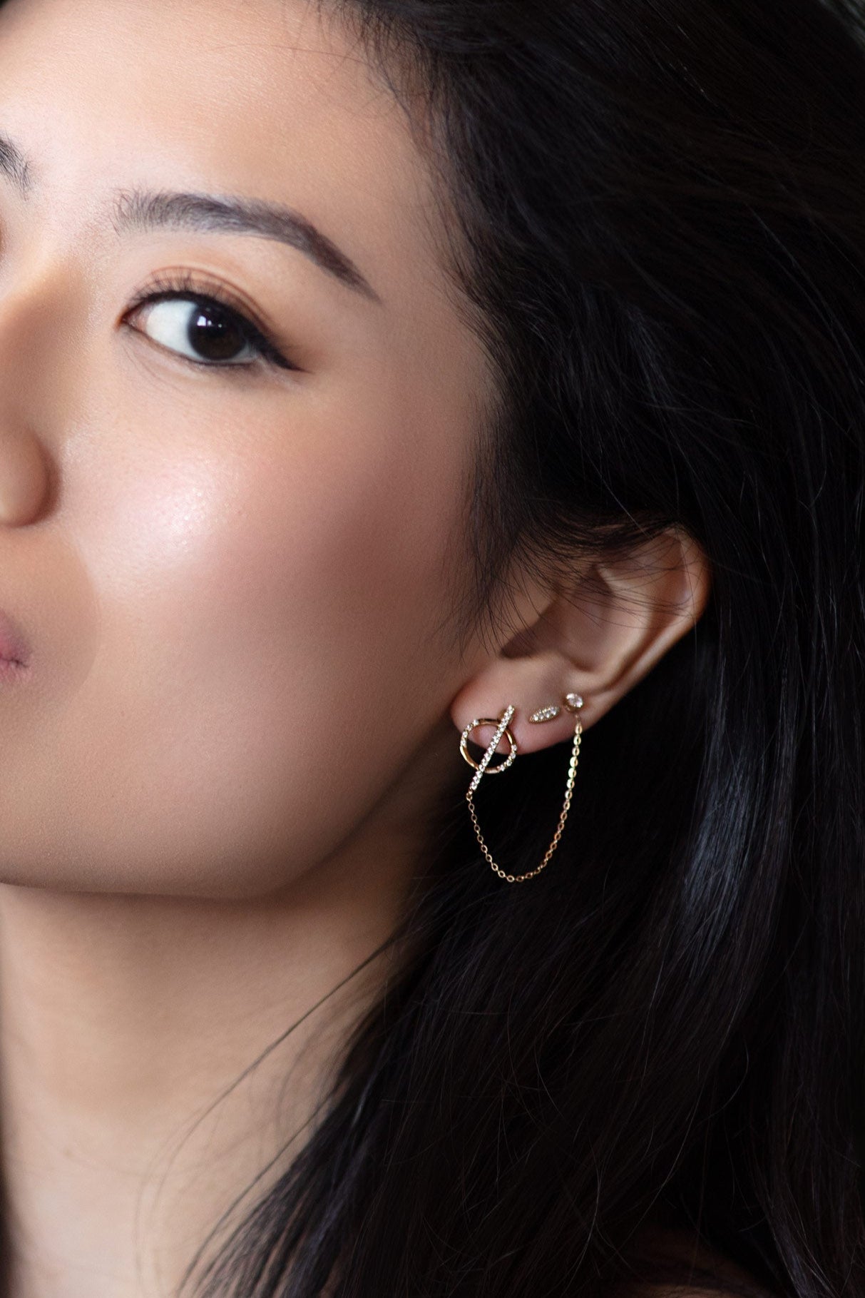 Close-up of a person wearing gold and diamond earrings with a soft beige background