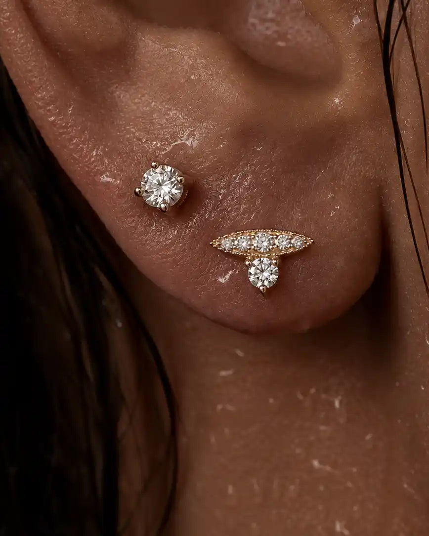 Close-up of a person's ear showcasing two gold-toned stud earrings: one round brilliant-cut diamond stud and one butterfly-shaped stud with a marquise-cut diamond and small round diamonds.
